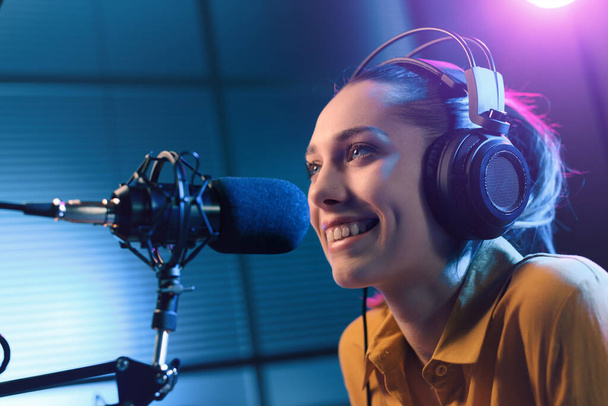 Young smiling woman wearing headphones and talking into a microphone at the radio station, entertainment and communication concept - Φωτογραφία, εικόνα