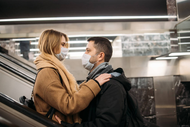 Side view of hugging couple in medical masks on escalator in subway. - Foto, Bild