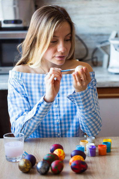 Праздники, ручная работа и концепция творчества - Счастливая молодая женщина рисует пасхальное яйцо
. - Фото, изображение