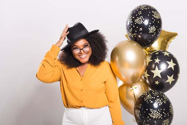 Tatiller, doğum günü partisi ve eğlenceli konsept - Beyaz arka planda balonlarla şık görünen gülümseyen Afro-Amerikan genç kadın portresi. - Fotoğraf, Görsel