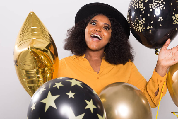 Tatiller, doğum günü partisi ve eğlenceli konsept - Beyaz arka planda balonlarla şık görünen gülümseyen Afro-Amerikan genç kadın portresi. - Fotoğraf, Görsel