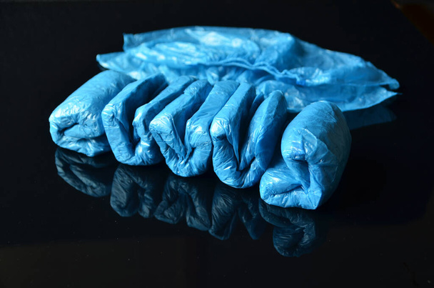 Concepto de Coronavirus.Cubiertas de zapatos desechables azules médicos sobre fondo negro. Reglas de higiene durante la epidemia de coronavirus
.  - Foto, imagen