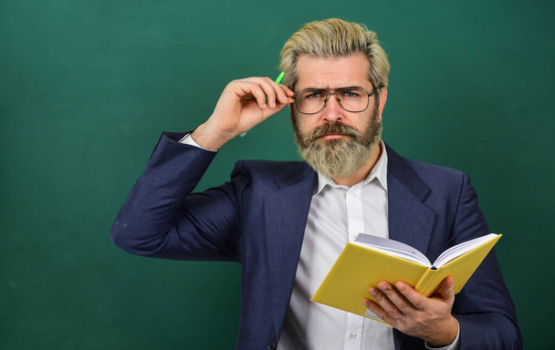 Selecting appropriate courses. Teacher with book explain topic. Man in front of chalkboard. College and high school. Literature subject. Reading books. Teacher with textbook. Experienced teacher - Φωτογραφία, εικόνα