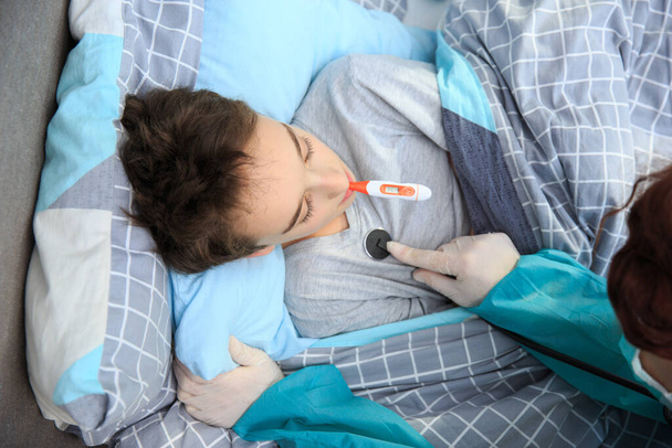 Sick boy with thermometer laying in bed. Sick child with fever and illness in bed. Flu. Cold, Children and illness COVID-2019 disease concept. Home quarantine at Coronavirus - 写真・画像