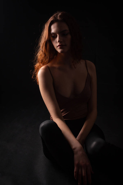 Πορτρέτο ενός νεαρού σγουρού κοριτσιού σε ένα σκοτεινό στούντιο - Φωτογραφία, εικόνα