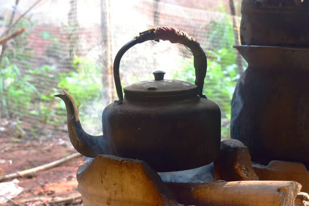 A régi alumínium vízforraló a tűzhelyen füsttel a vidéki konyhában. - Fotó, kép