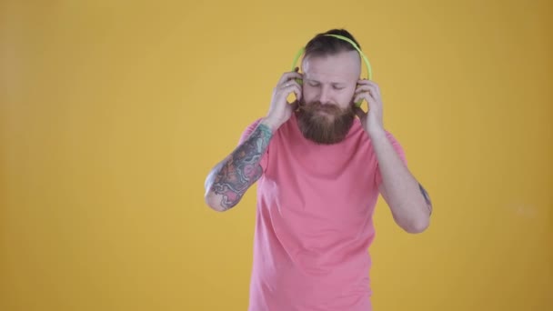man in pink t-shirt listening to music and headphones, on yellow background - Metraje, vídeo