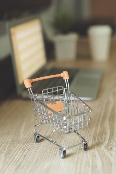 Online shopping concept, Shopping cart with blurry laptop on the desk - Foto, imagen