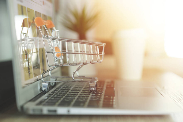 Online shopping concept, Shopping cart with blurry laptop on the desk - Fotó, kép