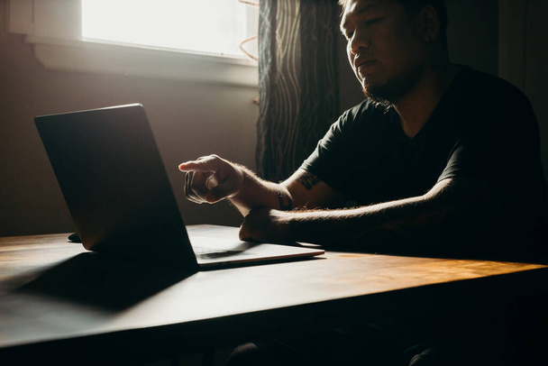 Азиат, работающий на ноутбуке в тёмной зоне. Указание на экран
. - Фото, изображение