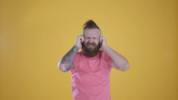 man in pink t-shirt listening to music and headphones, on yellow background - Filmati, video