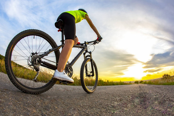 Hermoso ciclista deportivo monta una bicicleta en la carretera contra el telón de fondo de la hermosa naturaleza y la puesta de sol. pasatiempos y deporte
 - Foto, Imagen