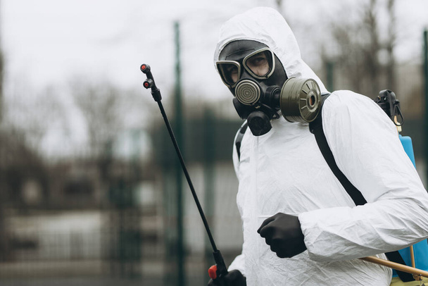 コロナウイルス流行中の町の複合施設での清掃と消毒消毒作業のための専門チーム感染予防と流行の制御保護スーツとマスク. - 写真・画像