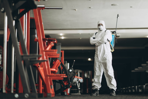 Cleaning and Disinfection in crowded places amid the coronavirus epidemic Gym cleaning and disinfection Infection prevention and control of epidemic. Protective suit and mask and spray bag - Φωτογραφία, εικόνα
