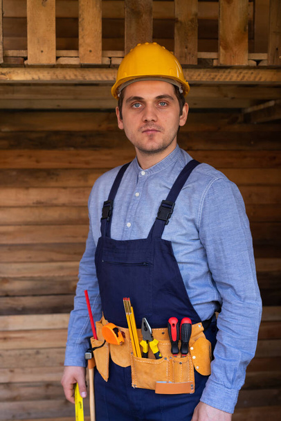 Portrait of a confident young workman wearing yellow helmet, blue uniform - DIY renovation concept - Foto, immagini