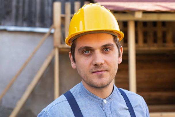 Portrait of a confident young workman wearing yellow helmet, blue uniform - DIY renovation concept - Valokuva, kuva