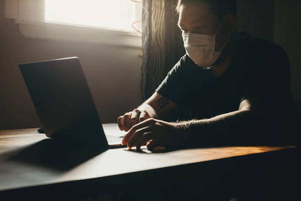 Un asiatico uomo in medico maschera lavoro su laptop in dark area
. - Foto, immagini