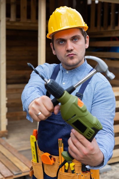 Handsome young repairman holding construction tools in front of wooden background - Foto, Imagen