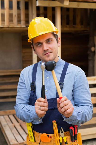 Handsome young repairman holding construction tools in front of wooden background - Valokuva, kuva