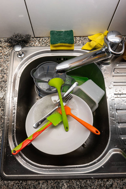 Кухонная раковина, полная грязной посуды, моющая сетка из губчатой проволоки и посуда, вид сверху 2020
 - Фото, изображение