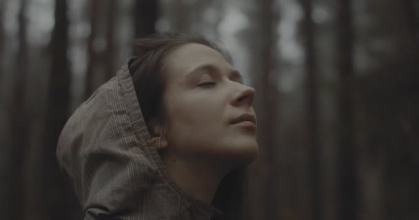 Portret młodej dziewczyny stojącej w lesie i marzącej o czymś. Piękna kobieta bez makijażu spogląda w niebo i cieszy się przyrodą. nastolatka dziewczyna twarz otwarcie i odzież oczy na zewnątrz - Materiał filmowy, wideo
