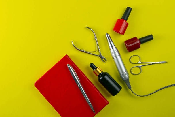 A set of cosmetic tools for manicure and pedicure. Manicure scissors, cuticles, saws, miller and red notebook stand on a yallow background. Top views with clear space. - Photo, Image
