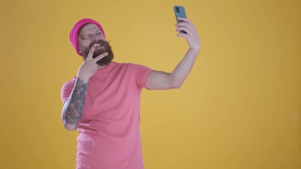 Caucasian man taking selfie on phone,making funny faces on yellow background - Video, Çekim