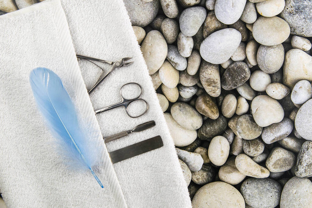 Een set cosmetische hulpmiddelen voor manicure en pedicure. Manicure schaar, nagelriemen, zagen op witte handdoek met een blauwe pen staan op zee stenen achtergrond. Top uitzicht met duidelijke ruimte. - Foto, afbeelding