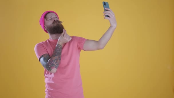 Caucasian man taking selfie on phone,making funny faces on yellow background - Záběry, video