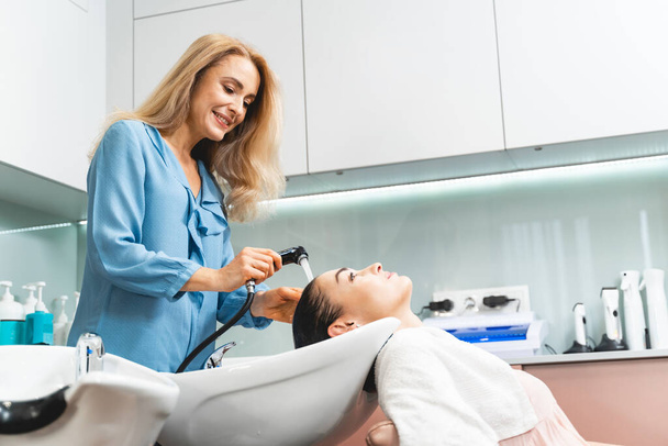 Positive delighted blonde hairdresser washing hair in sink - Zdjęcie, obraz