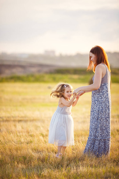 mom hold little daughter in dress jumping in field - Foto, Imagem