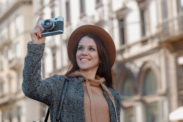 Beautiful brunette tourist girl holds a camera in her hands and looks into the lens. - Fotó, kép