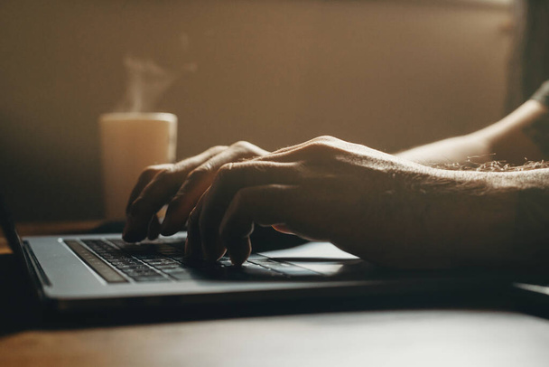 Вид сбоку крупным планом человека, использующего ноутбук в темной области. Работа сверхурочно с кофе
. - Фото, изображение