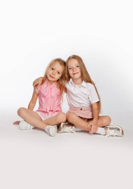 Two cute girlfriends are sitting hugging and legs crossed on the floor in the studio. Bright portrait. - Photo, image