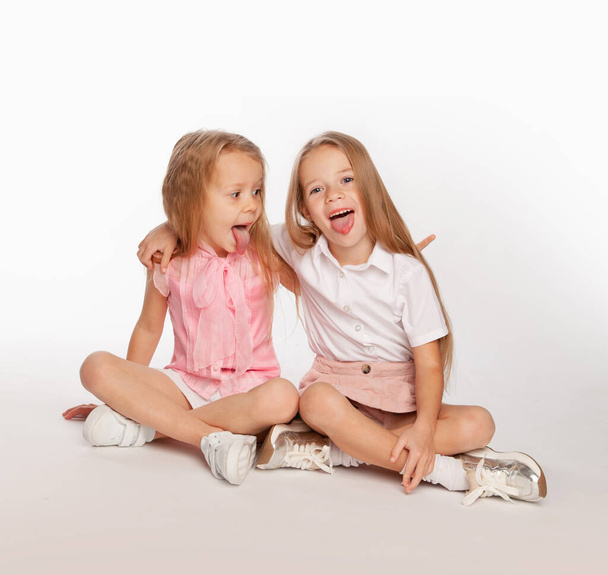 Két barátnő ül keresztbe tett lábbal, és megmutatják egymásnak a nyelvüket. - Fotó, kép
