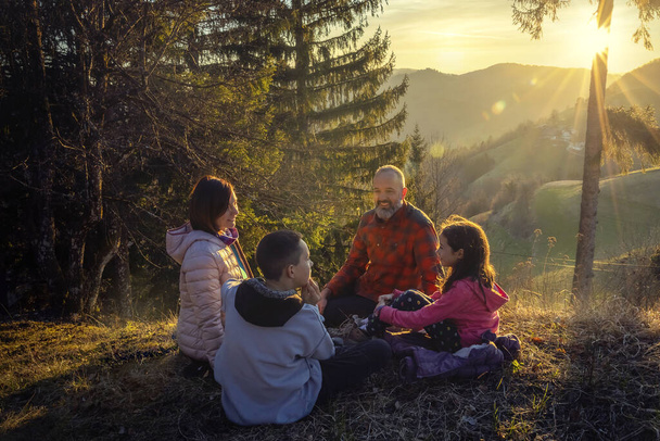 田舎の家族のピクニック。日没の牧草地で楽しむアクティブな家族. - 写真・画像