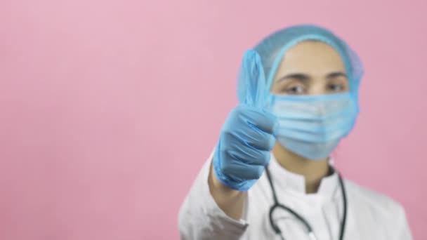 Жінка-лікар в медичній масці для обличчя і медичні рукавички, що показують великі пальці вгору. Не хвилюйтеся, будьте щасливі. Після ковадла-19 або постпандемічного періоду. Святкування перемоги над коронавірусом
 - Кадри, відео