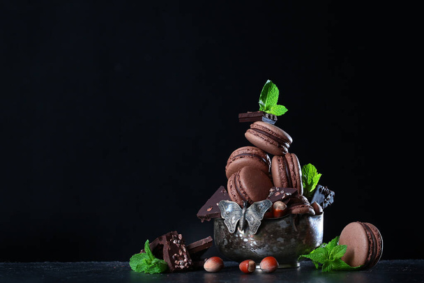 Chocolate macaroons in a vintage vase on a black background. Macaroons with nuts and chocolate chunks. Photo on a dark background. Copy space. - Valokuva, kuva