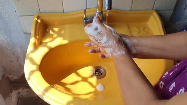 käsien pesu saippualla lähellä keltaista pesuallasta päivällä korostaen sormen vinkkejä viruksen ja infektion ehkäisemiseksi
 - Materiaali, video
