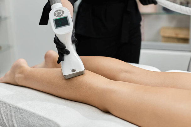 primer plano del brazo esteticista que masajea la pierna de la mujer usando guantes negros en la clínica de belleza
 - Foto, Imagen