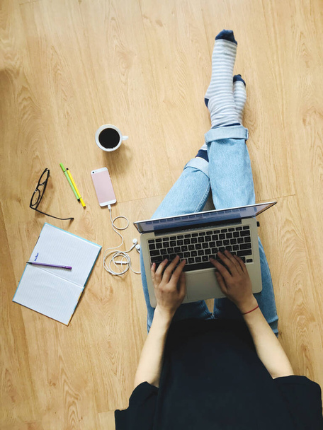 Egy lány ül a földön egy laptoppal. A közelben van egy notesz, bögre kávéval és telefonnal. - Fotó, kép