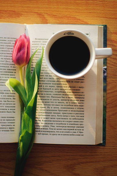 Café aromático fuerte y sabroso en la ventana con un libro interesante y tulipanes rosados. El sol de la mañana brilla en un libro y el café aromático, y hermosos tulipanes rosados frescos se encuentran cerca
 - Foto, imagen