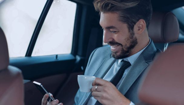 Businessman drinking coffee in car with phone in hand - Fotó, kép