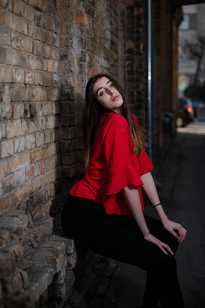Girl in a red blouse and a gray cardigan on the background of the old brick wall - Фото, зображення