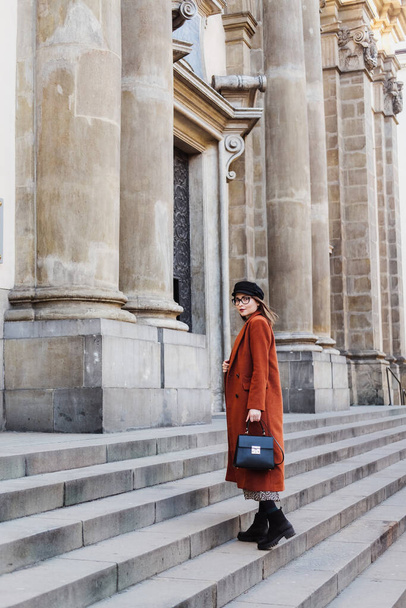 Beautiful young woman in a terracotta coat walks in the old city. - Fotó, kép