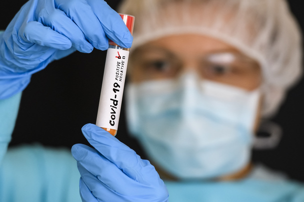 Frau im Schutzanzug hält Reagenzglas mit positivem Ergebnis infiziert mit Coronavirus COVID - 19. Foto-Illustration. - Foto, Bild