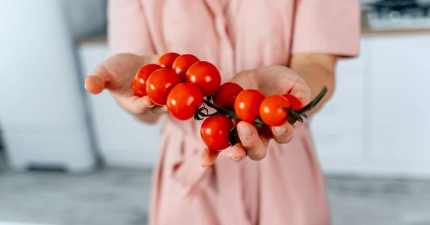 Woman holding ripe cherry tomatoes in hands. Kitchen background. Cropped image. Healthy food. - Foto, immagini