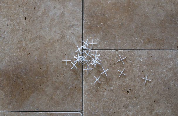 een wit plastic kruis voor het leggen van tegels, op de achtergrond van stenen tegels - Foto, afbeelding