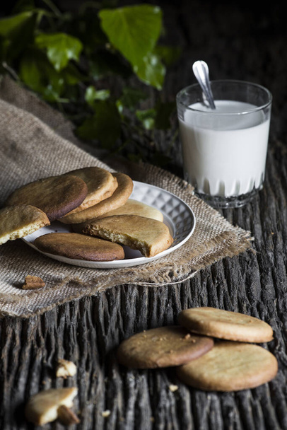 Печенье ручной работы на тарелке на деревенской деревянной доске и со стаканом молока
 - Фото, изображение