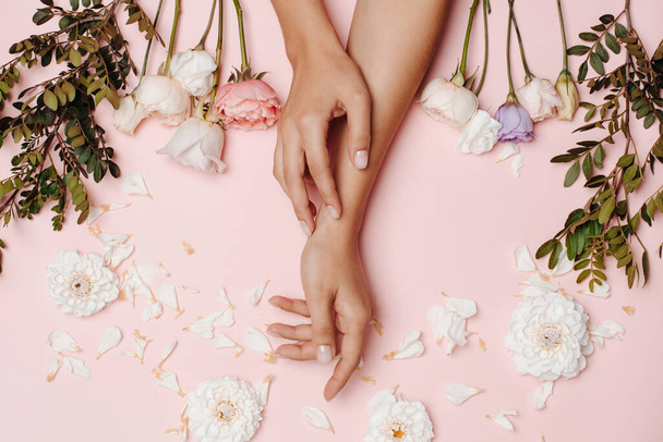 Руки жінки і білі, рожеві і фіолетові квіти і зелені гілки, пелюстки на рожевому тлі
. - Фото, зображення